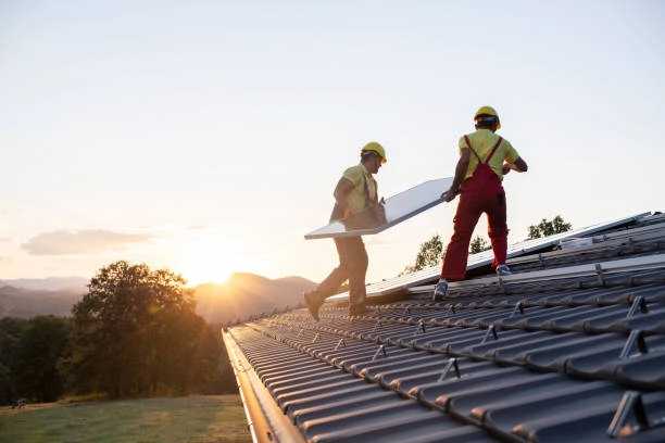 Two workers installing solar panels on a roof during sunset. -exterior home remodel