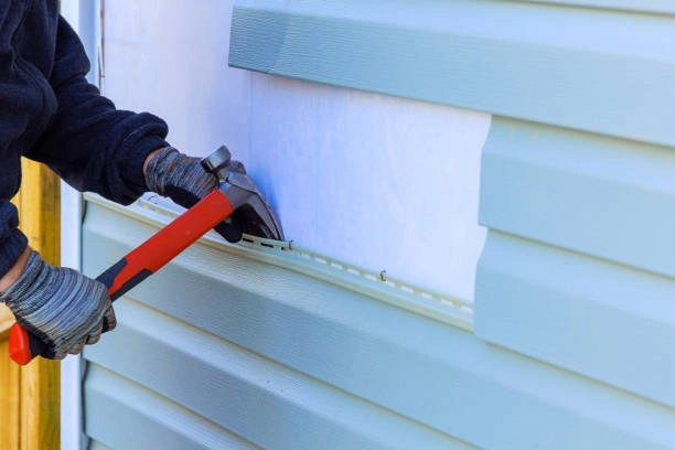 A worker installing vinyl siding on a house using a hammer. -exterior house remodel