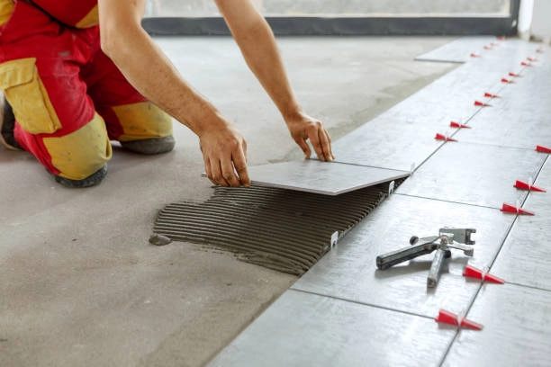 Worker installing tile flooring with adhesive and leveling spacers. -flooring installation contractors