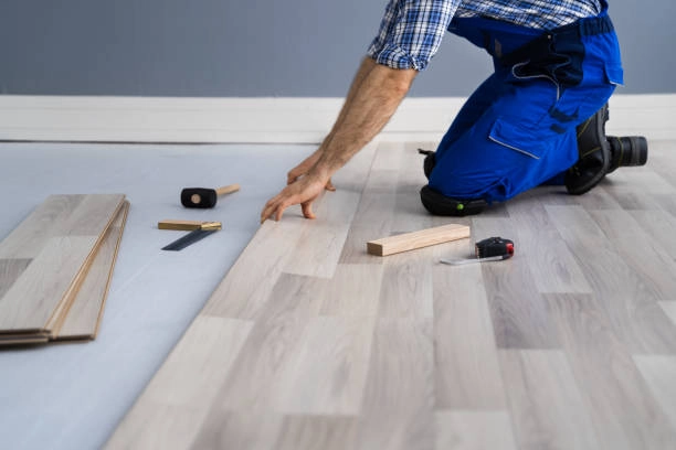 Worker installing laminate flooring with tools and wooden spacers. -flooring installation contractors