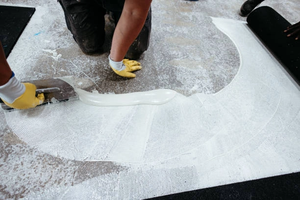 Worker applying adhesive with a trowel before laying carpet tiles. -commercial flooring contractors