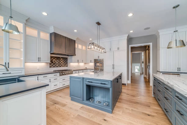 Spacious modern kitchen with white cabinetry, marble countertops, and hardwood flooring. -hardwood floor contractors